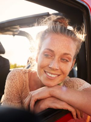 Millennial white couple on a road trip driving in open top car, women leaning on car door, close up