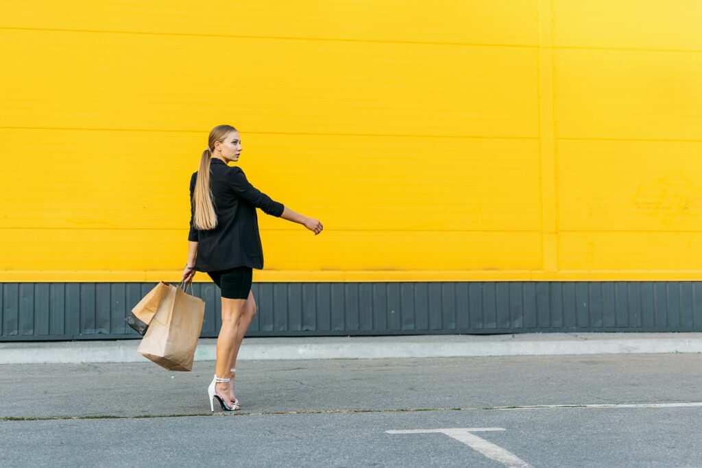 Shopping, sale concept. Stylish fashionable young woman walking and holding shopping bags on yellow